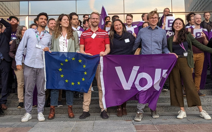 Acto de lanzamiento de la lista europea de candidatos a las puertas del Parlamento Europeo con una bandera de la UE y otra de Volt